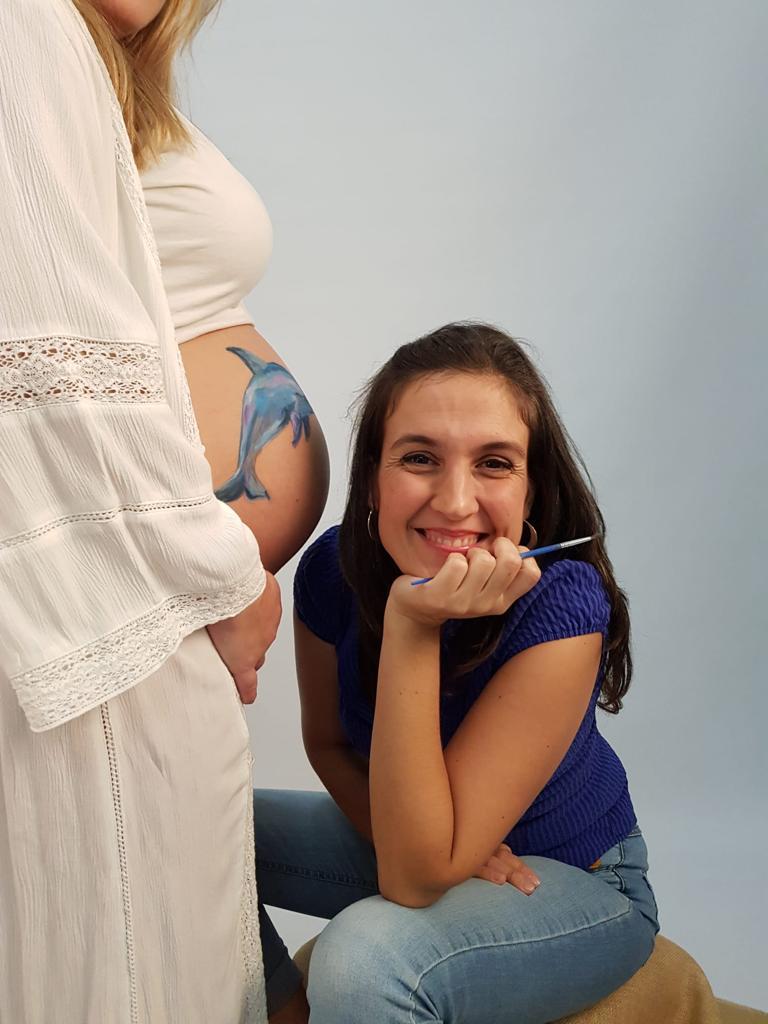 Chica pintando delfín en vientre de embaraza
